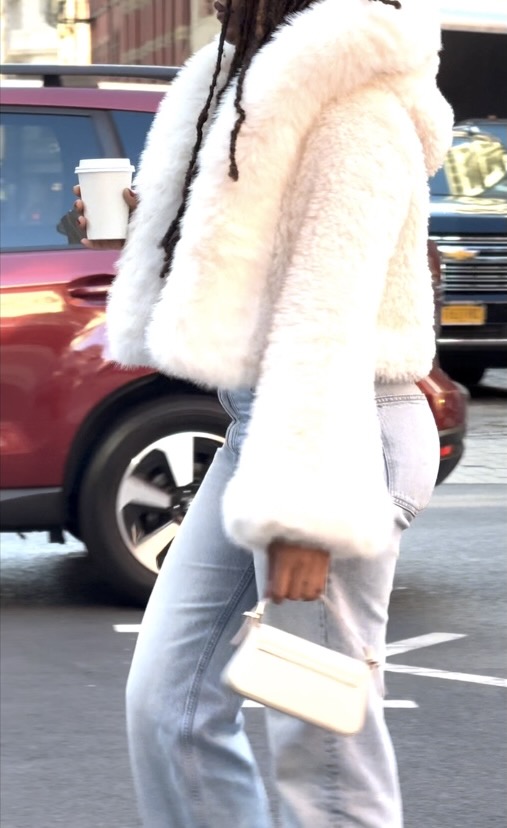 White faux fur jacket with light wash jeans, white clutch, and coffee cup.