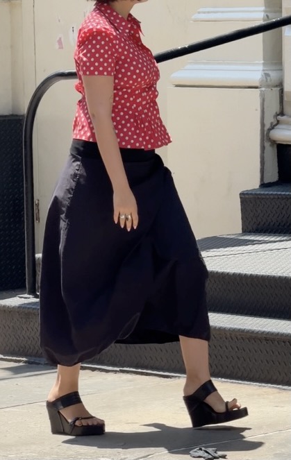 Red polka-dot button-up shirt, black draped wide-leg pants, and black wedge sandals.