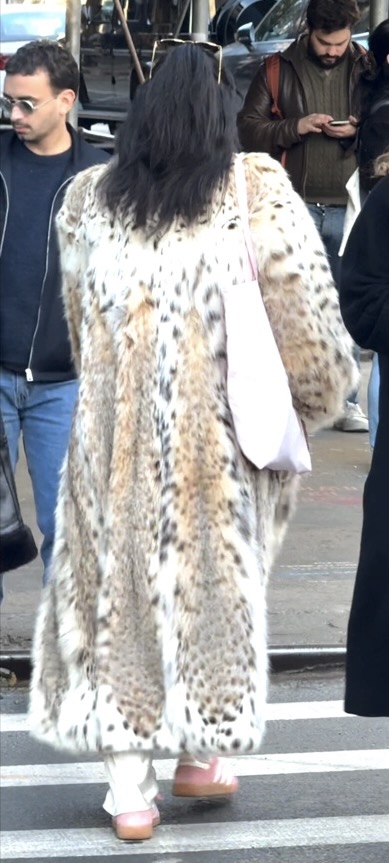 Long spotted fur coat with a pink tote bag and white pants.