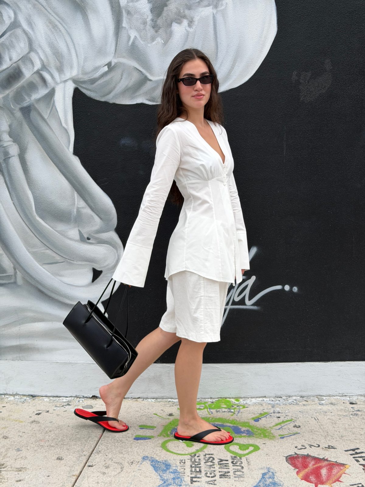 White V-neck button-up shirt and shorts, black sunglasses, black purse, and red-soled flip-flops.