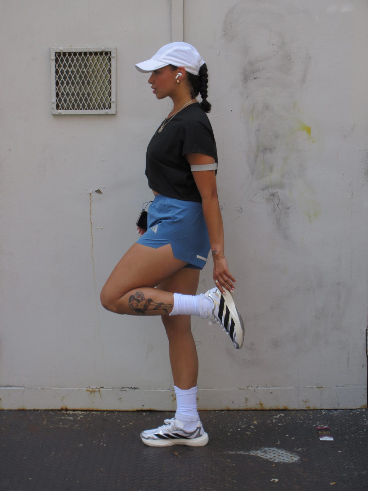 Black crop top, blue athletic shorts, white cap, and white sneakers.