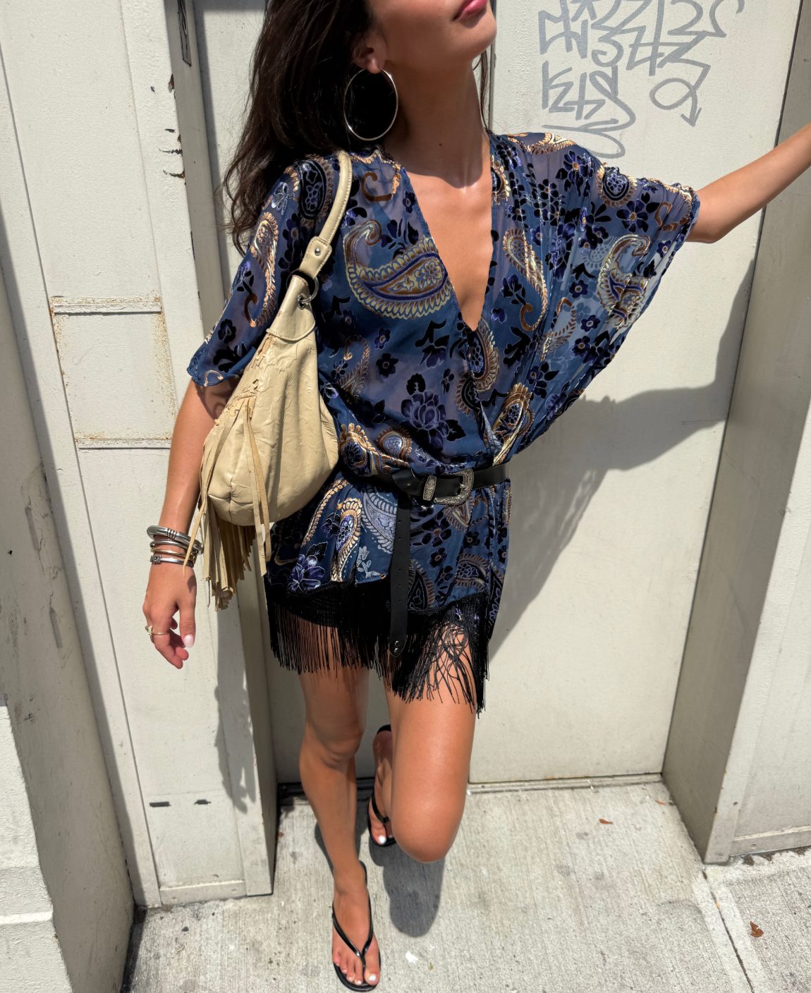 Blue paisley top with fringe skirt, black belt, tan bag, and flip-flops.