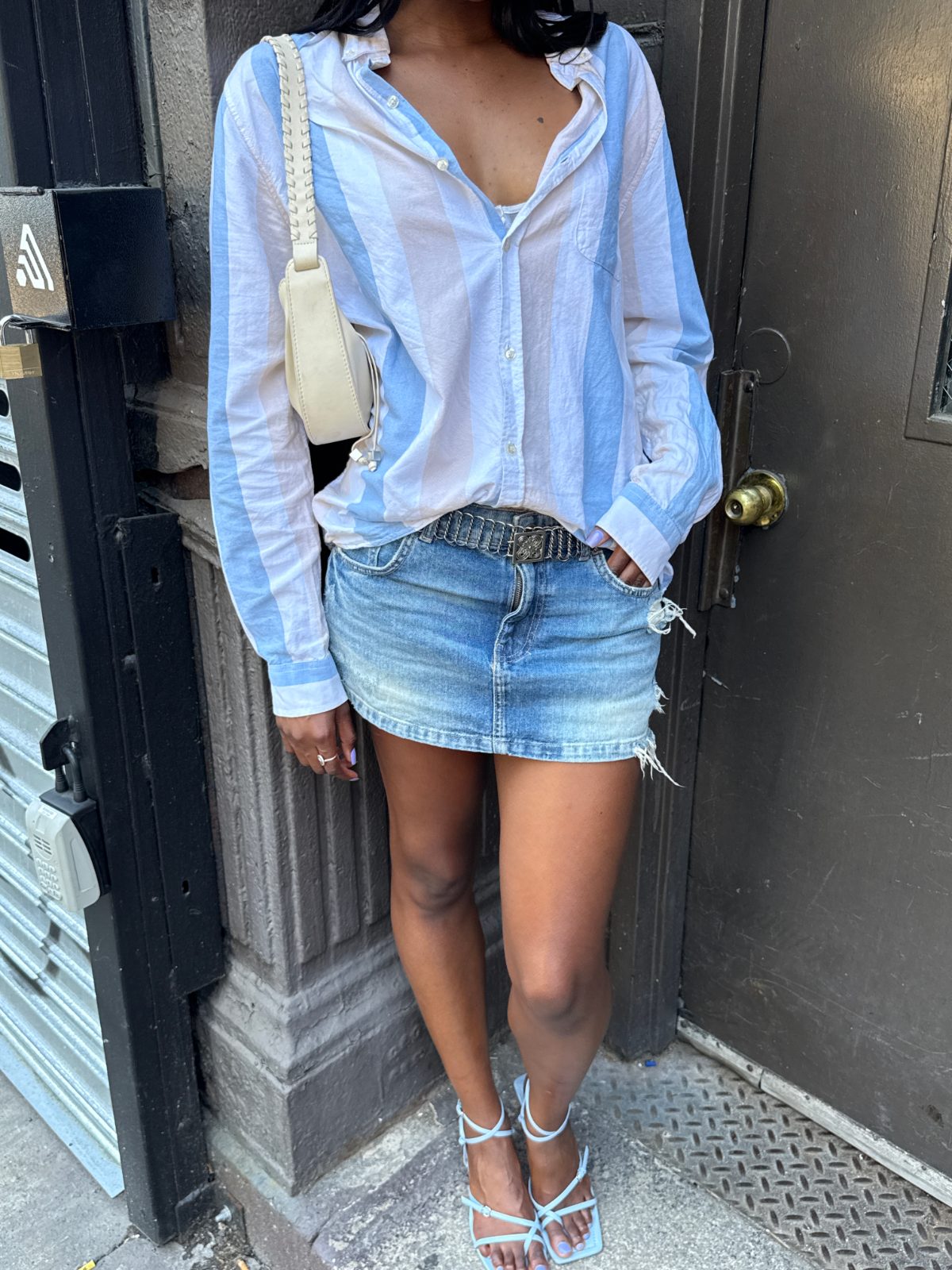 White and blue striped button-down, denim mini-skirt with silver chain belt, and blue strappy heels.