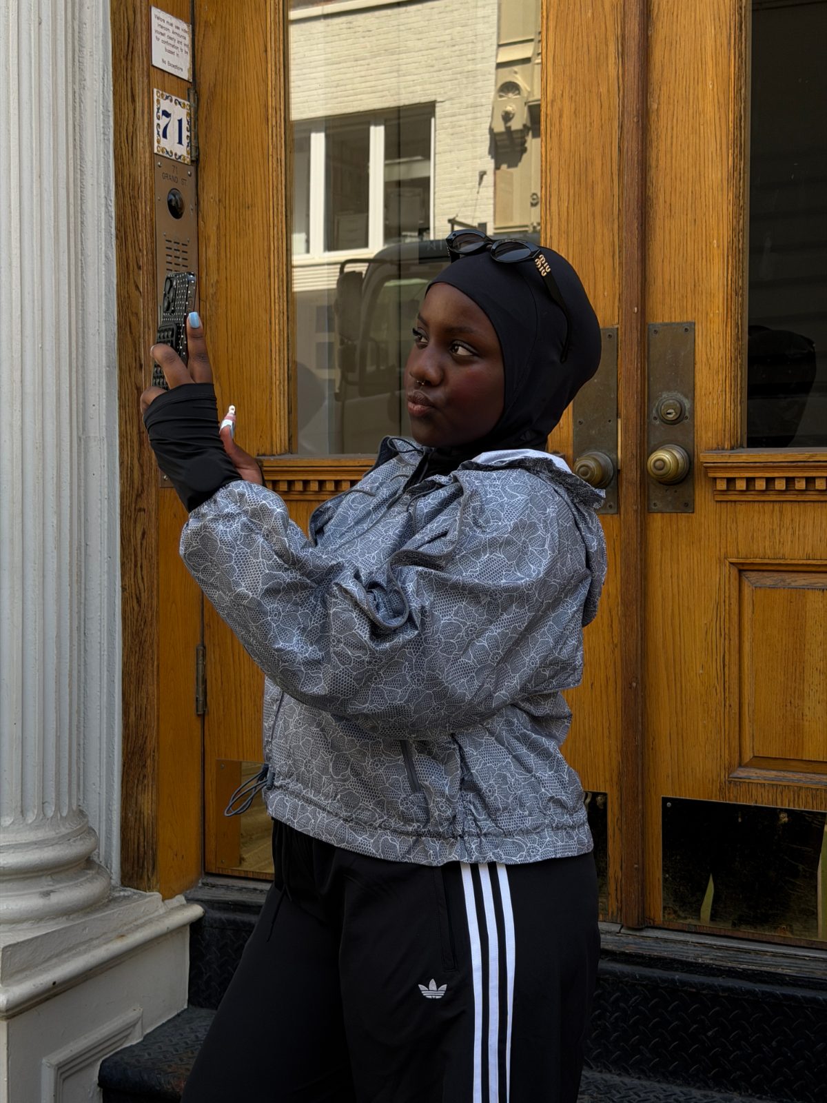 Gray patterned windbreaker, black hijab, and black Adidas track pants in urban setting.