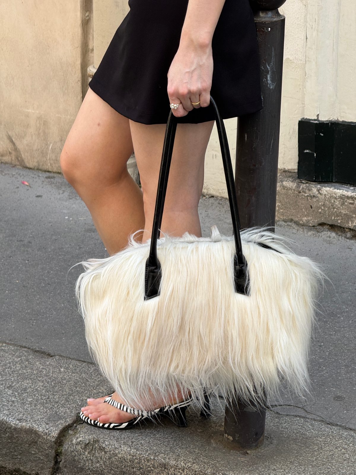 Black mini dress with white furry handbag and black and white striped flip-flops.